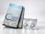 نمایی از بسته بندی لنز طبی فصلی کریستال کلیر (Gelflex Crystal Clear) با دوره تعویض یک تا سه ماهه، طراحی آسفریک و درصد آب ۵۵ درصد؛ عکاسی استودیویی با نورپردازی آبی و انعکاس نور روی سطح. عکس استودیویی لنز طبی بی رنگ فصلی کریستال کلیر Crystal Clear با دو محفظه لنز، بسته بندی BioMoist و نورپردازی آبی