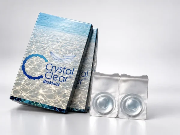 نمایی از بسته بندی لنز طبی فصلی کریستال کلیر (Gelflex Crystal Clear) با دوره تعویض یک تا سه ماهه، طراحی آسفریک و درصد آب ۵۵ درصد؛ عکاسی استودیویی با نورپردازی آبی و انعکاس نور روی سطح. عکس استودیویی لنز طبی بی رنگ فصلی کریستال کلیر Crystal Clear با دو محفظه لنز، بسته بندی BioMoist و نورپردازی آبی